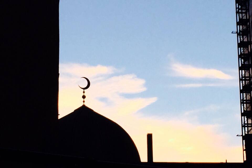 A mosque with a crescent moon on top, silhouetted against a sunset sky.