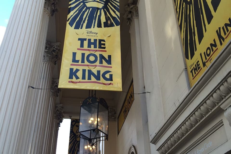 A building facade with columns and banners for 'The Lion King' musical.