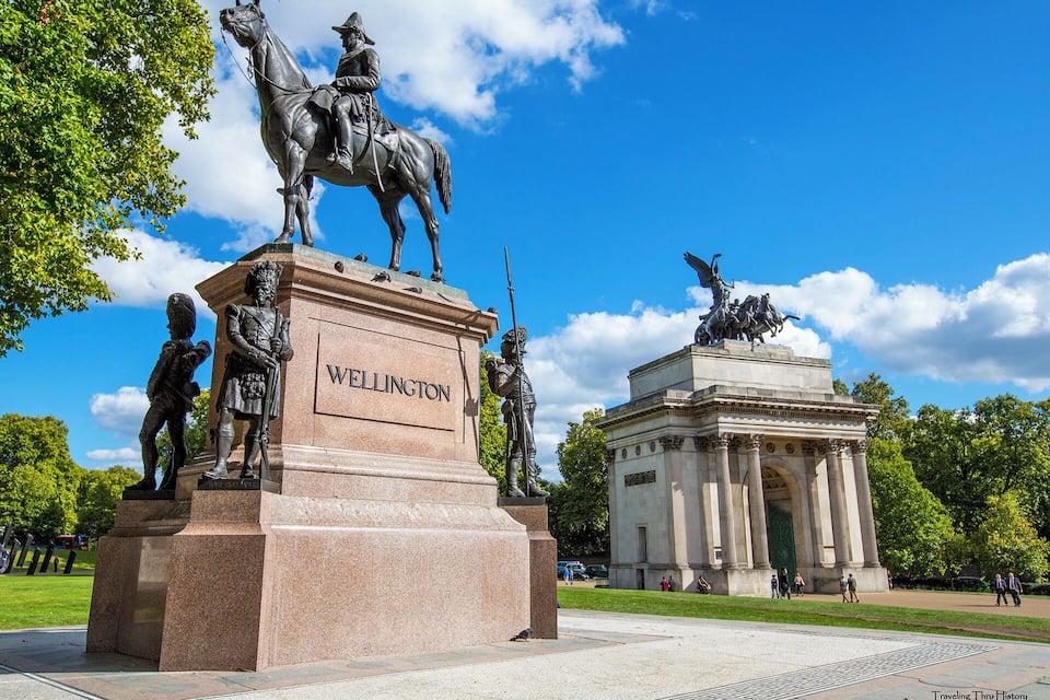 Monumento a Wellington con estatuas de figuras a caballo y soldados, rodeado de árboles y un cielo despejado.