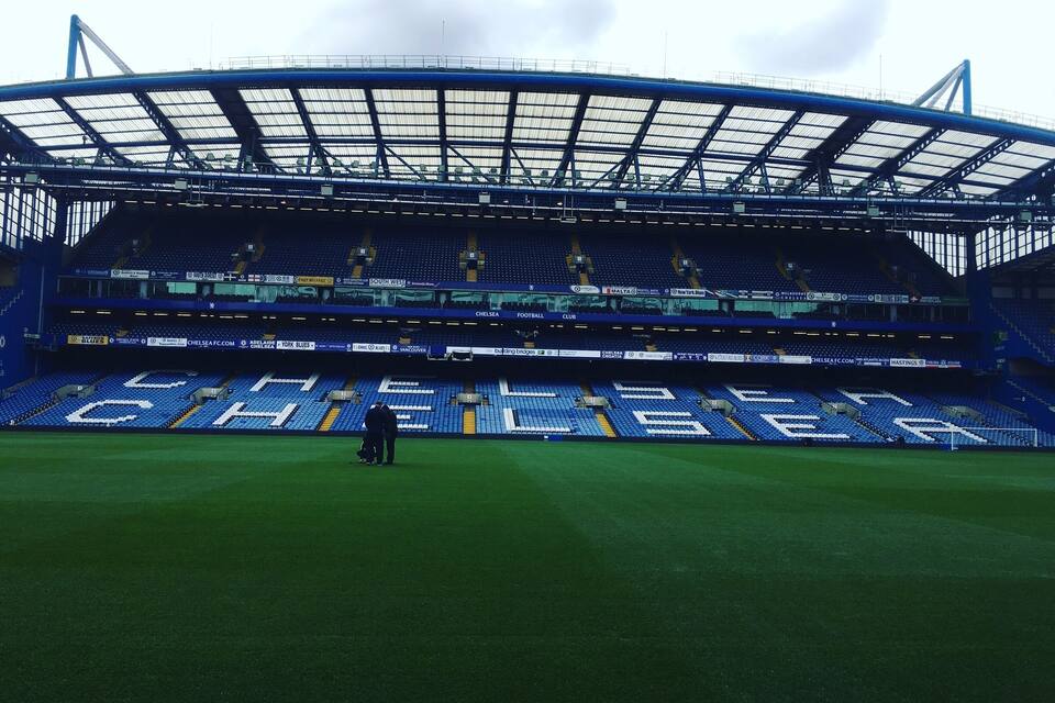 A large, empty stadium with blue seats and a roof structure.
