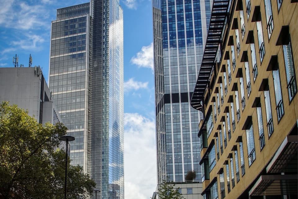 A city street with modern buildings, a clear blue sky, and a few cars on the road.