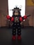 A robot with red and black parts, standing in a room with a window and a sign on the wall.