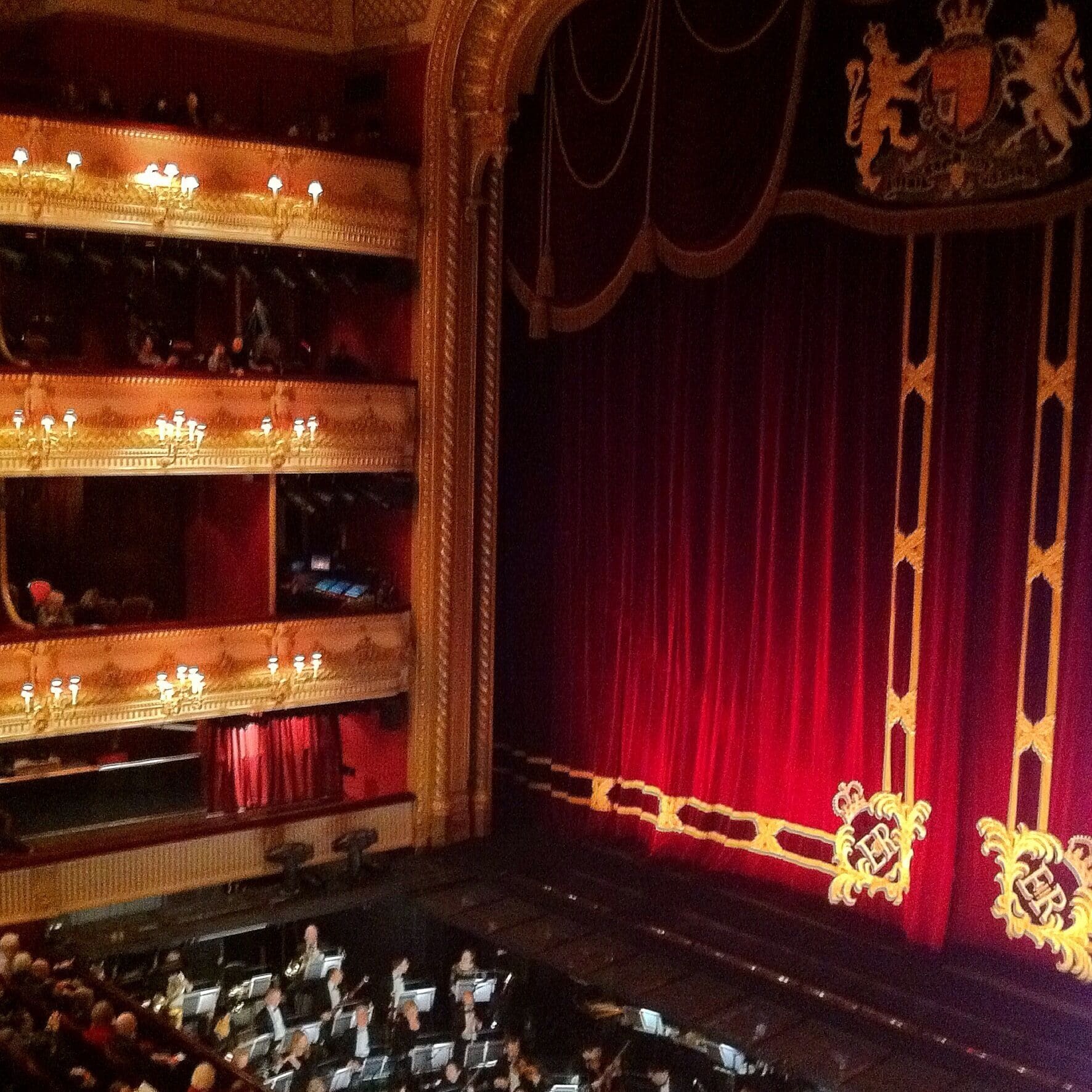 L’intérieur d’un théâtre somptueux, avec un rideau rouge et des éléments décoratifs dorés.