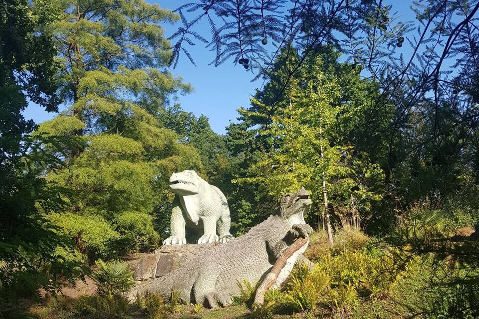 Una estatua de dinosaurio en un área boscosa bajo un cielo azul despejado.