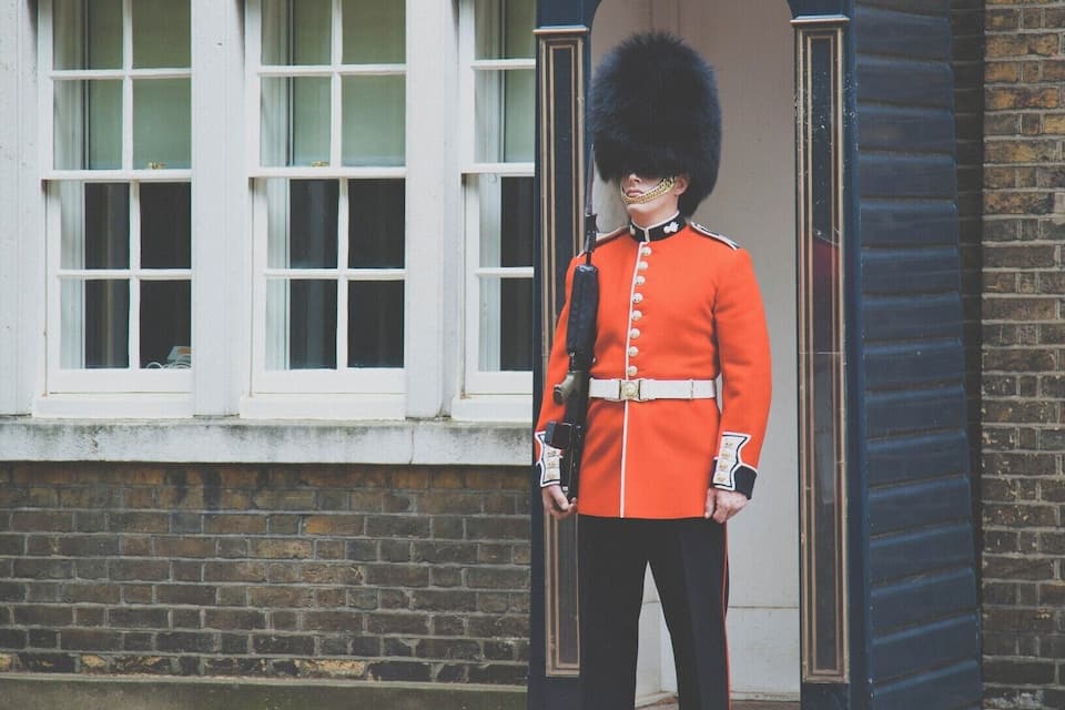 En vakt i en röd uniform står framför en traditionell byggnad med svart och guldfärgad fasad och ett vitt fönster.