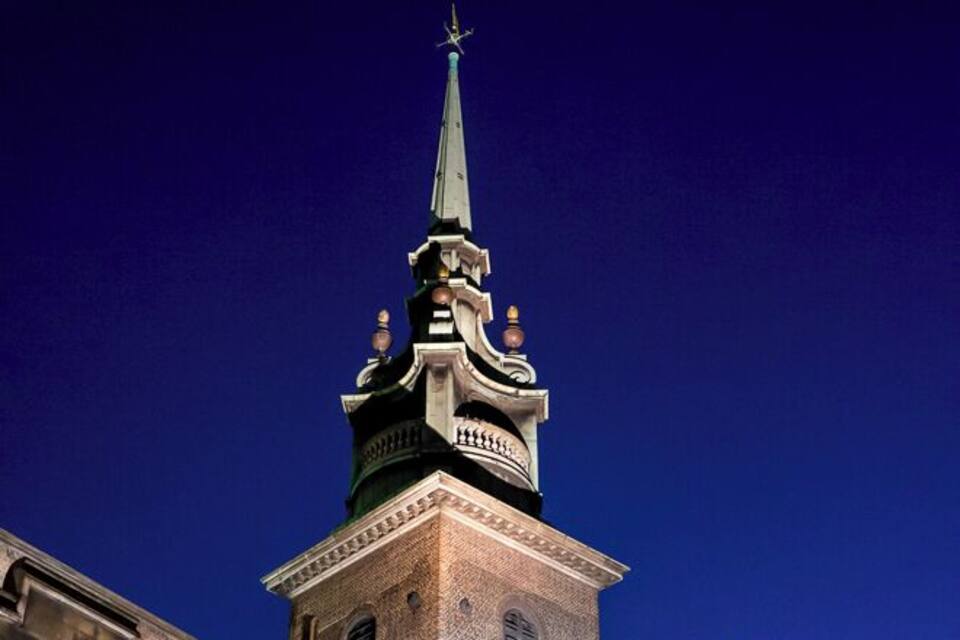 A church tower with a spire and clock at night.