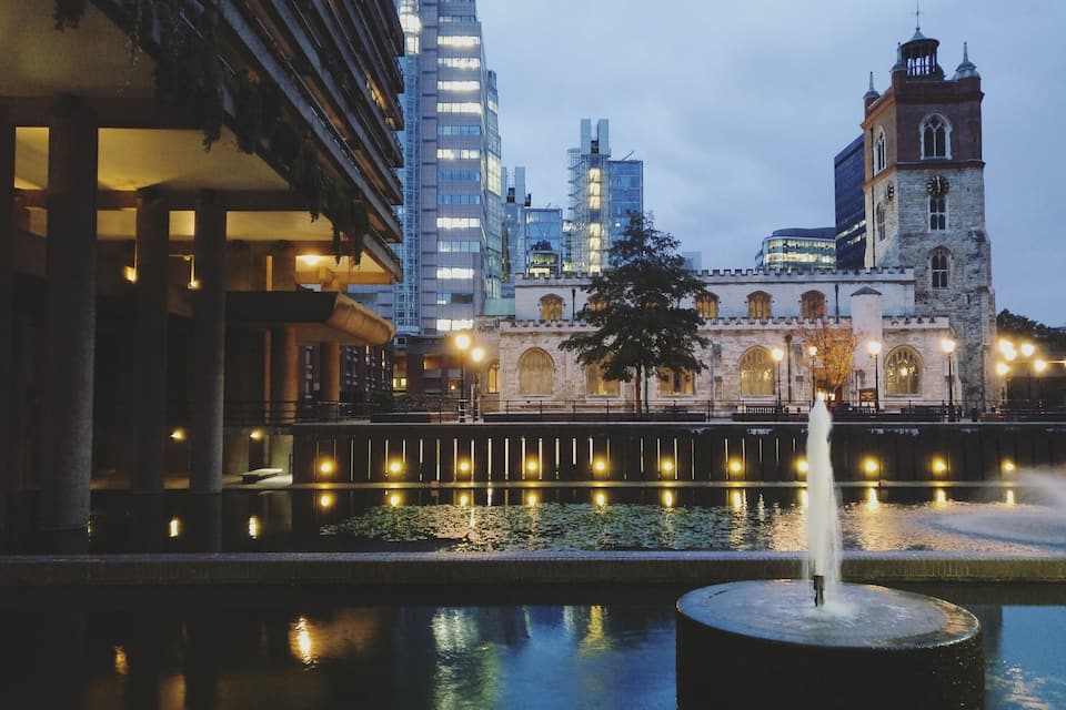 A historic building with a clock tower, a modern skyscraper, and a fountain in the foreground.