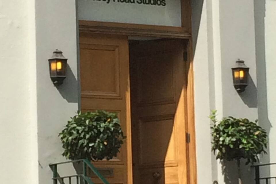 Ingresso di un edificio con un cartello che riporta "Abbey Road Studios" e due vasi con piante ai lati.