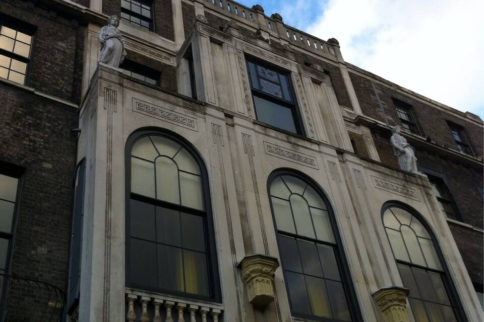 A historic building with large arched windows and statues on the roof.