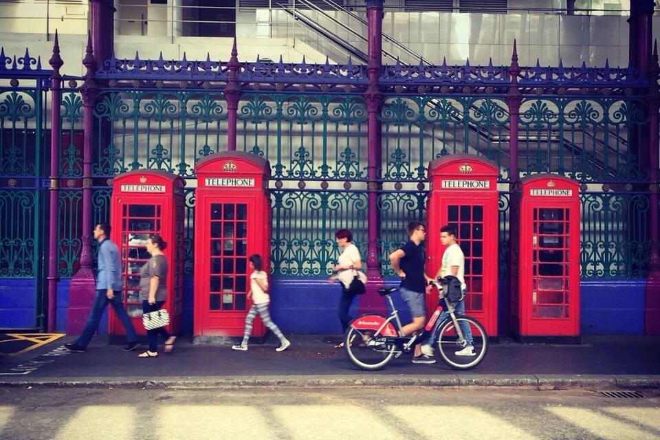 A row of red telephone booths with ornate metal railings and a staircase in the background.