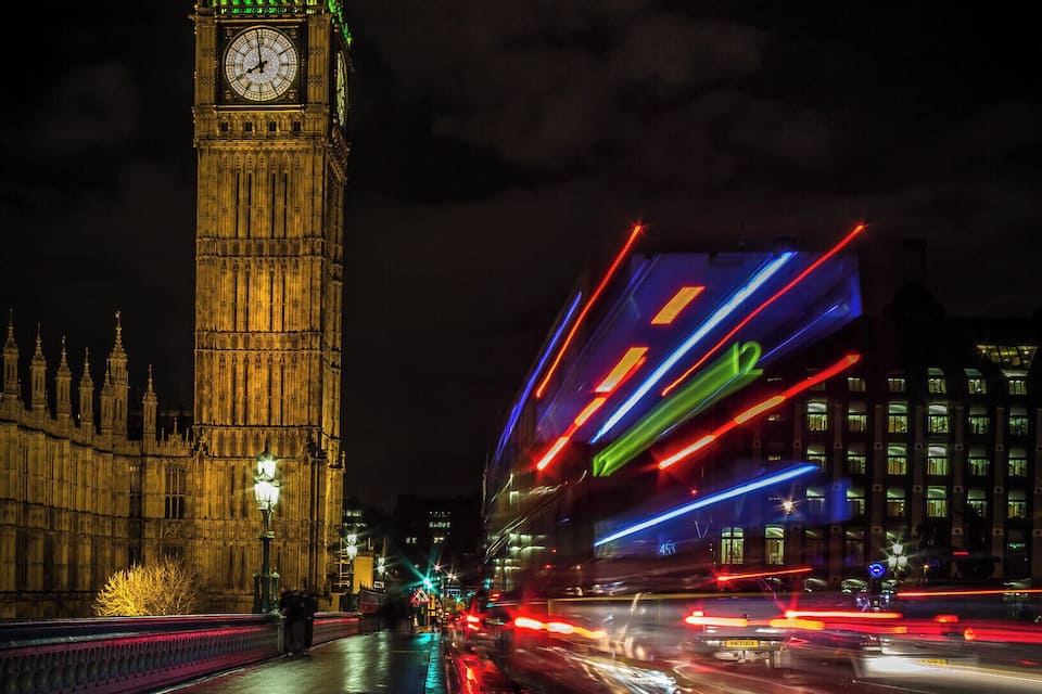 A nighttime view of the Big Ben clock tower with colorful light trails from passing vehicles.