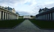 A grand neoclassical building with symmetrical columns and a central pathway leading to a large white structure in the background.