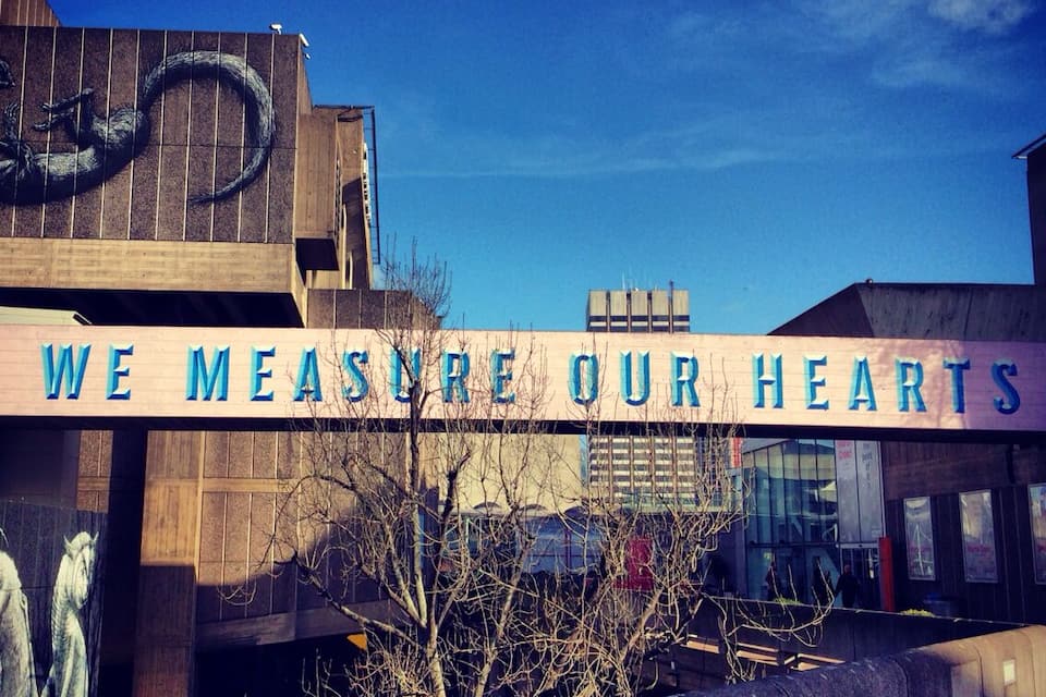 A building with a sign that reads "WE MEASURE OUR HEARTS" and a sculpture of a snake on the wall.