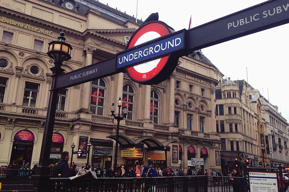 A busy London Underground entrance with a classic architectural building in the background.