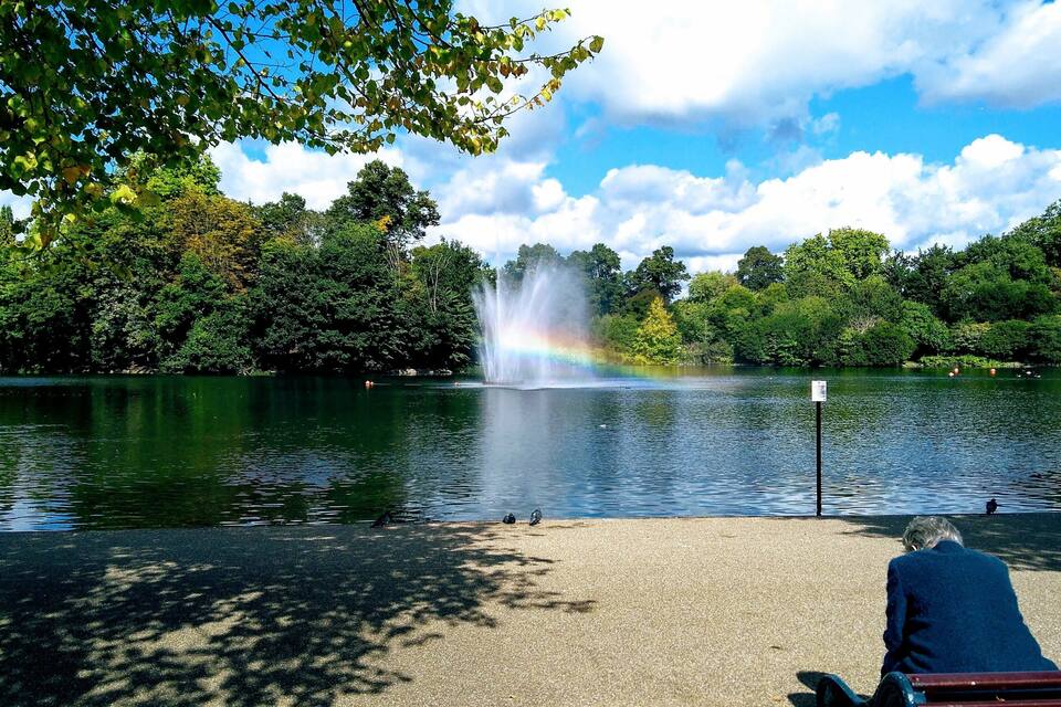 Ein Park mit einem Brunnen, einem Teich und einem Regenbogen.