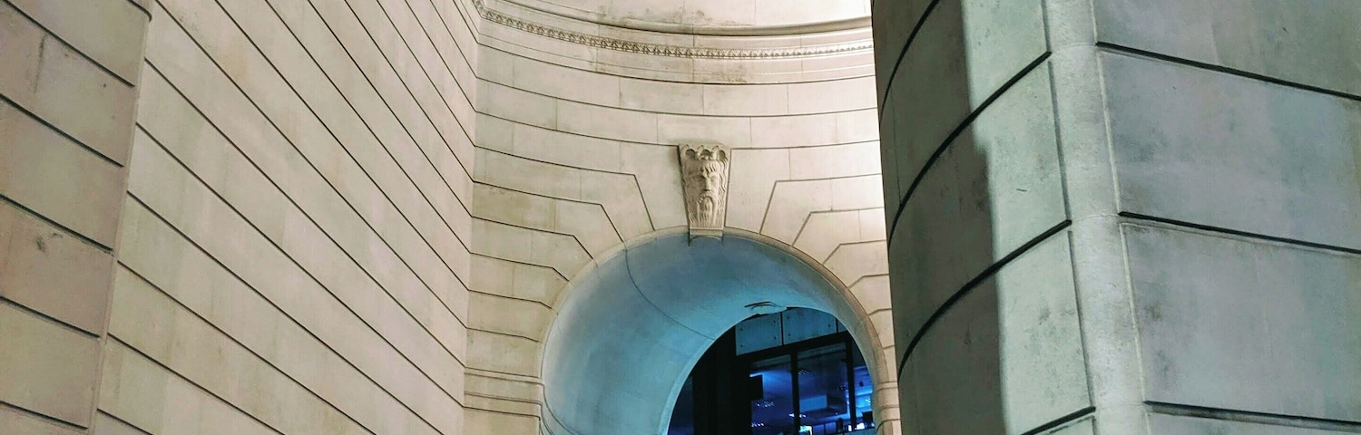 Ein steiner Torbogen mit der Aufschrift „WILLKOMMEN FÜR DIE BÜRGER“ und Blick in ein Gebäude mit blauer Beleuchtung.