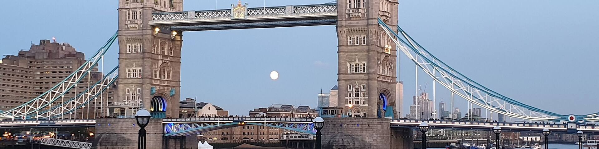 The Tower Bridge in London with the moon in the sky.