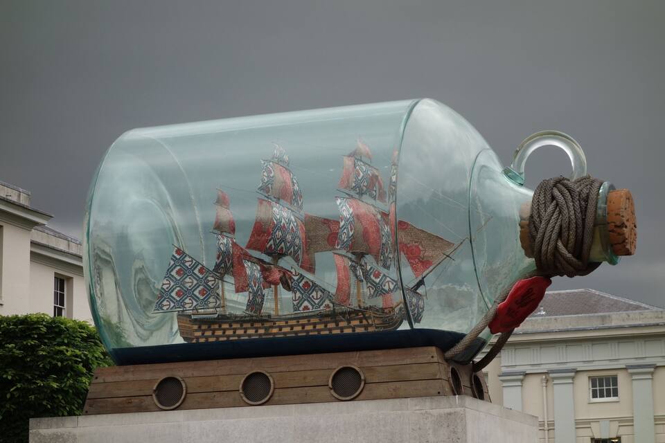 A glass bottle sculpture with a ship inside, set on a wooden base with circular cutouts.