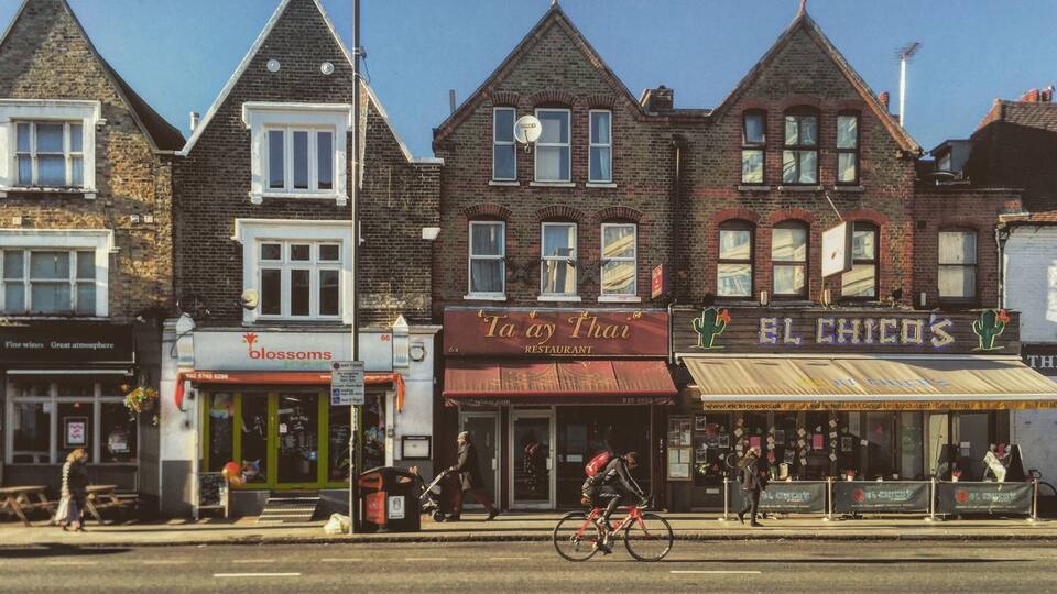 A street with Victorian-style buildings, a cyclist, and storefronts including 'Taay Thai Restaurant' and 'El Chico's'.