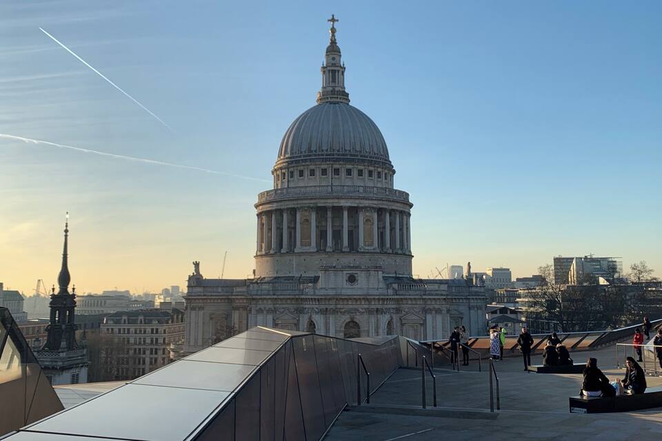 A large domed building with a cross on top, surrounded by modern buildings and a clear sky.