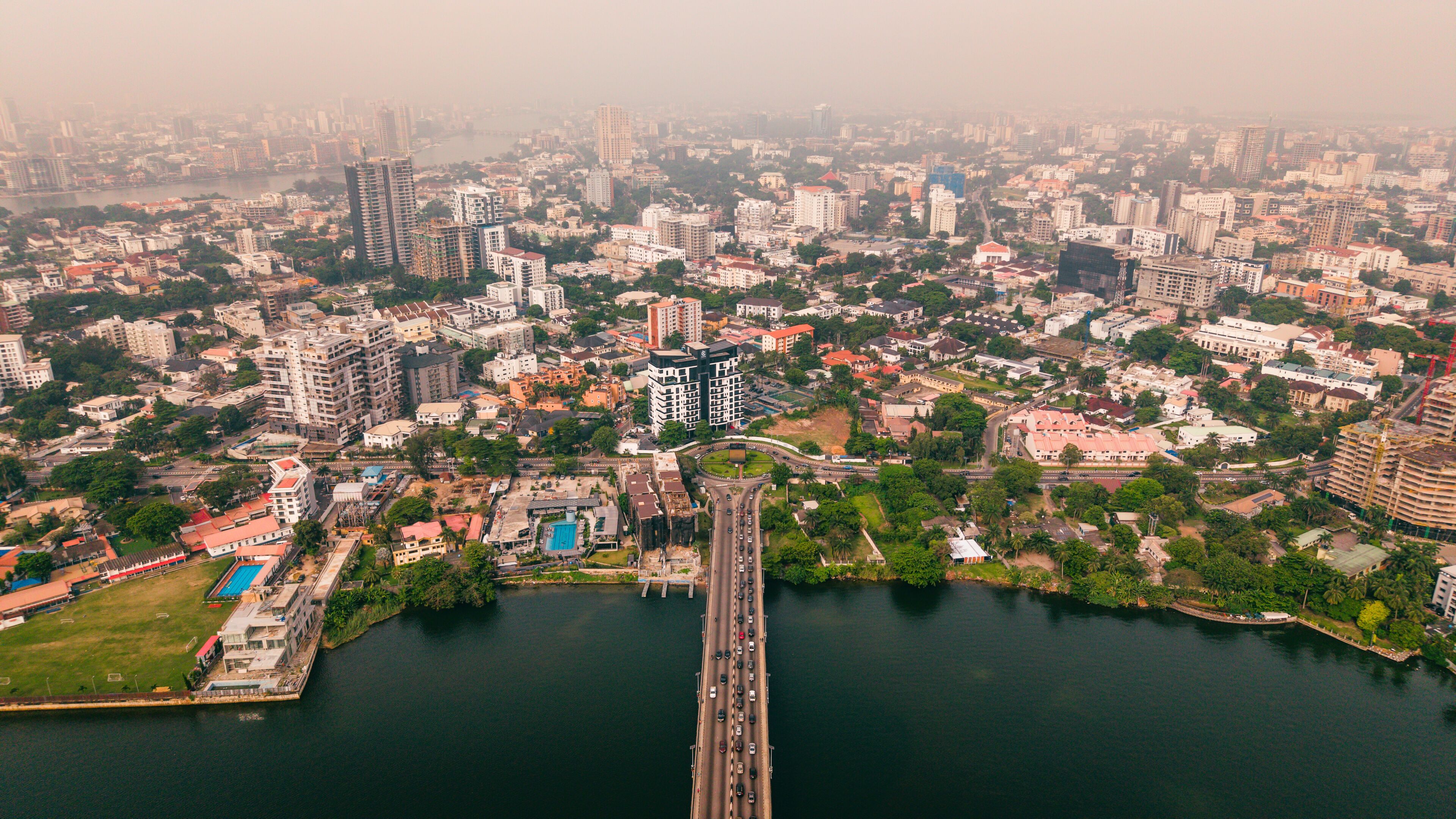 Aerial view of modern buildings meet serene waters, divided by a Lekki Ikoyi Link Bridge, creating a vibrant urban contrast, Lagos, Nigeria.