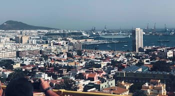 Un paisaje urbano costero con un crucero destacado en el puerto, un edificio blanco grande y una montaña al fondo.