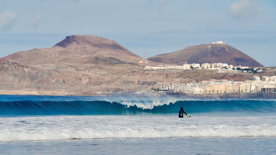 A surfer on a wave with mountains and a coastal town in the background.