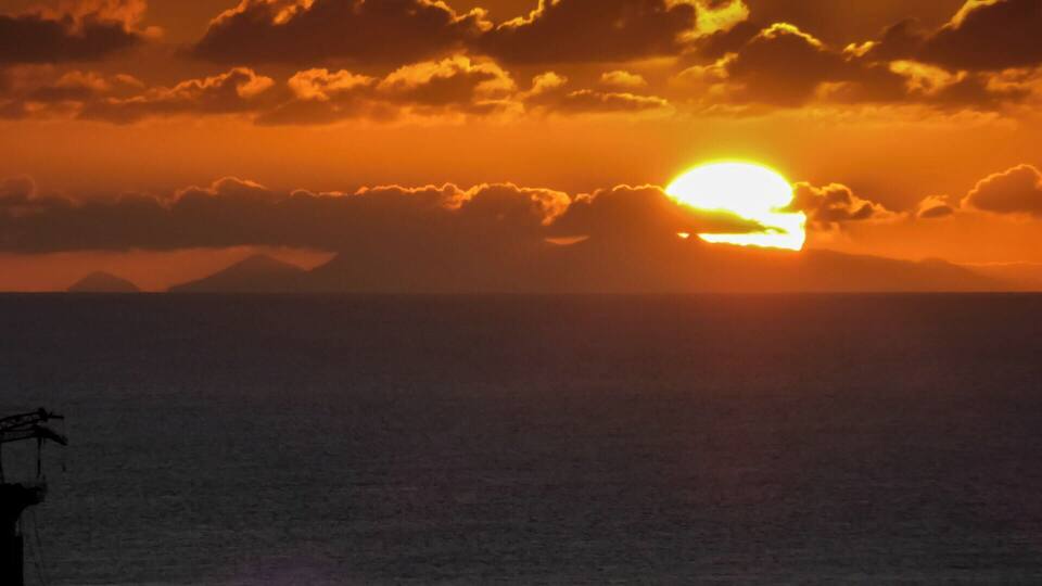 A sunset over the ocean with clouds and distant mountains.