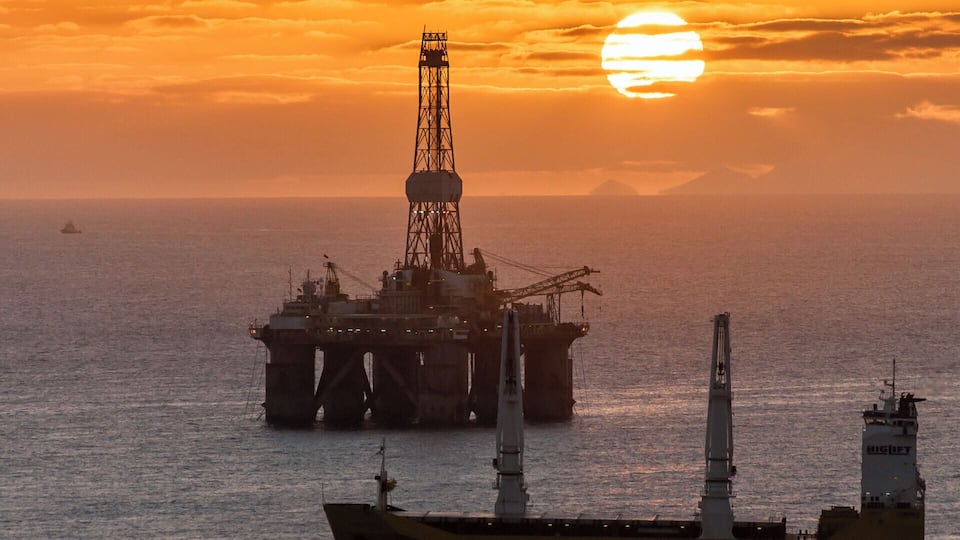 An offshore oil platform with a large ship in the foreground during sunset.
