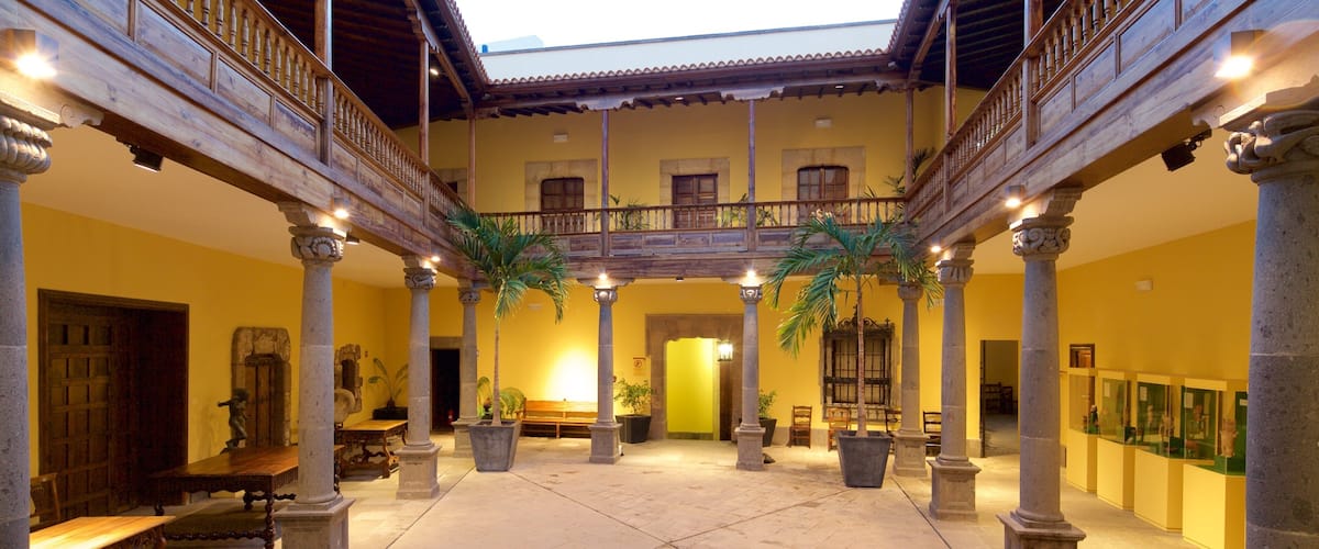 A courtyard with a wooden balcony, columns, and potted plants.