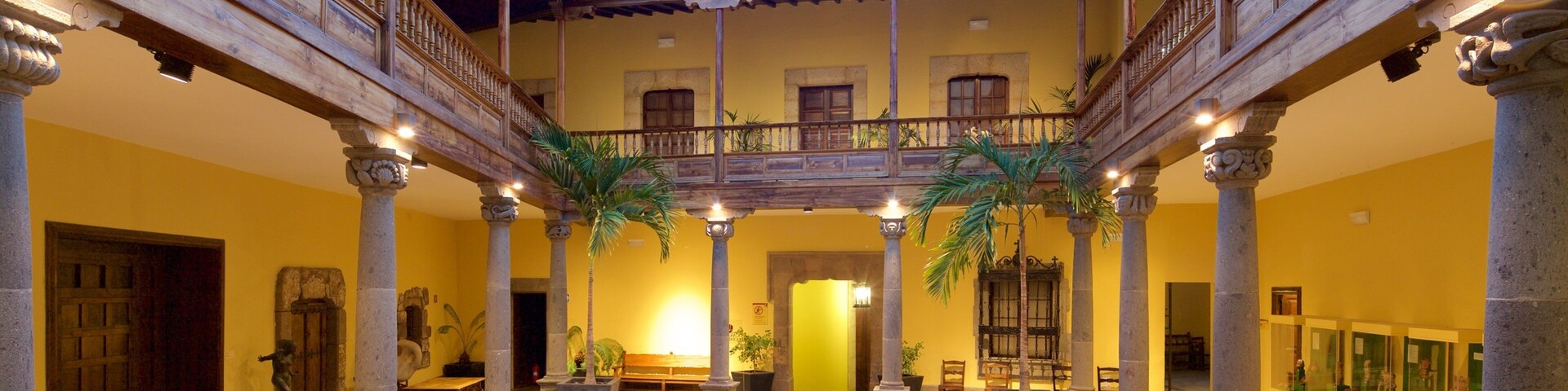 A courtyard with a wooden balcony, columns, and potted plants.
