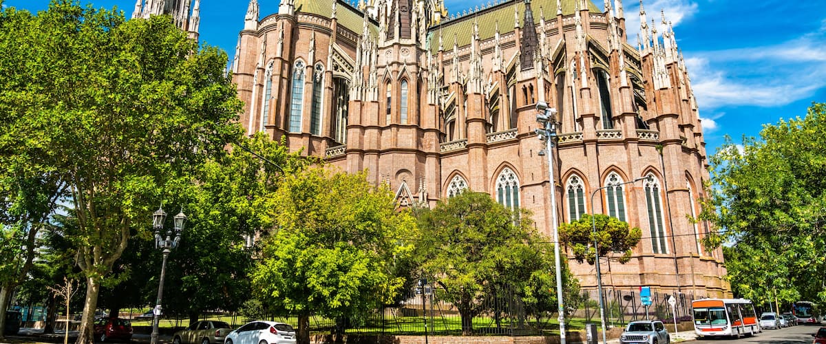 A large, ornate cathedral with intricate spires and a green roof, surrounded by lush trees and a clear blue sky.