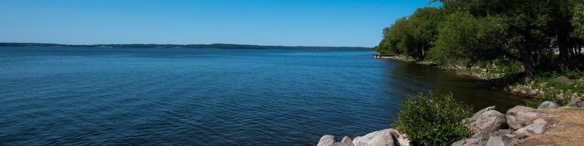 Un lago tranquilo con aguas azules y cristalinas, rodeado de costas rocosas y árboles verdes frondosos.