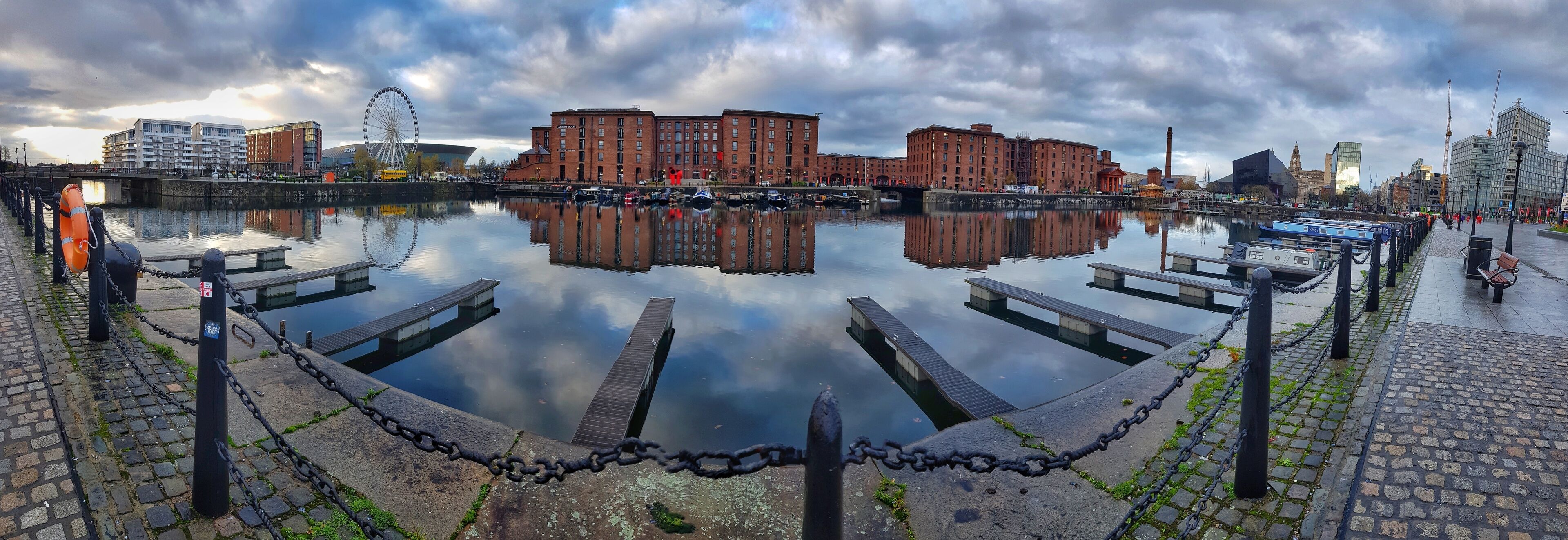 A calm waterfront with a clear reflection of buildings and a Ferris wheel.