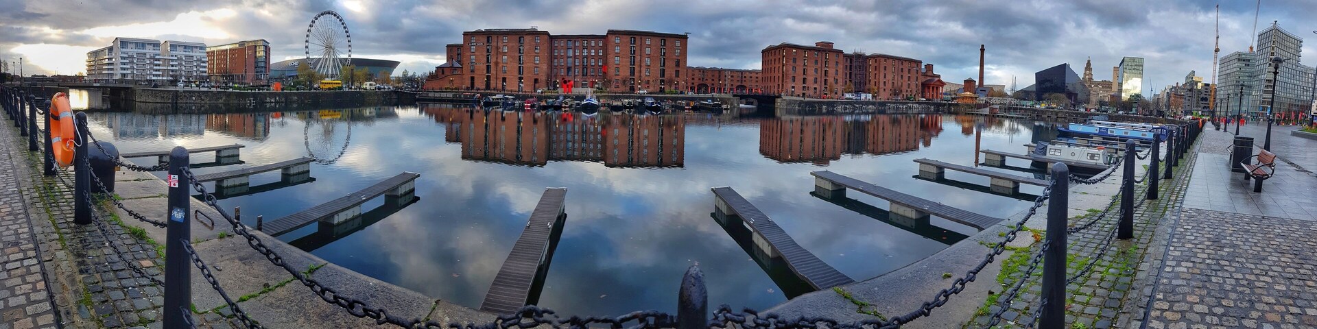 A calm waterfront with a clear reflection of buildings and a Ferris wheel.