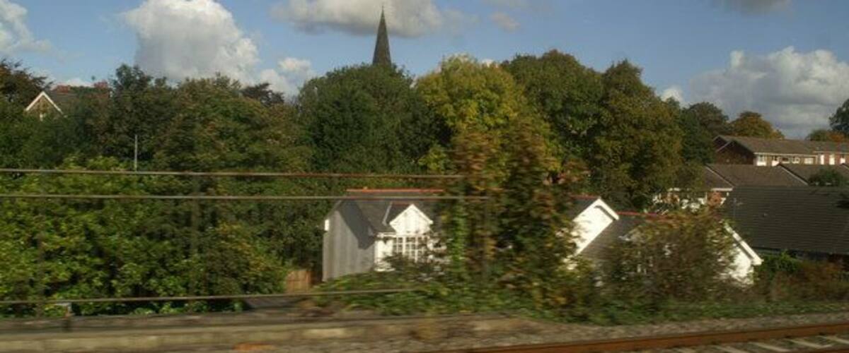 A railway track with a church spire in the background, surrounded by trees and houses.