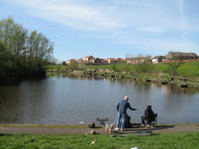 A calm lake with people fishing and a dog on the shore.