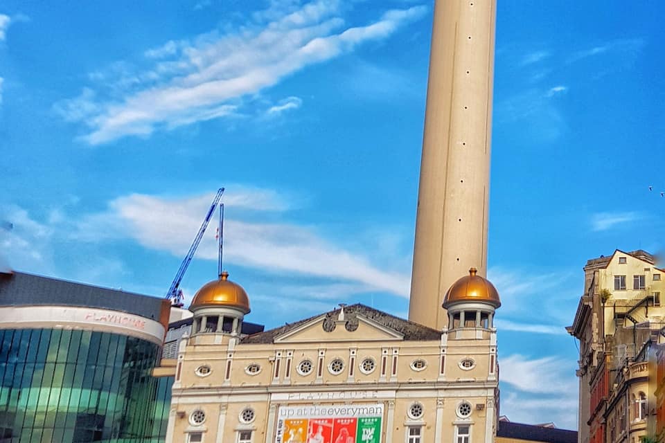 A tall tower with a pink dome and a radio city sign, surrounded by historic buildings and a clear blue sky.