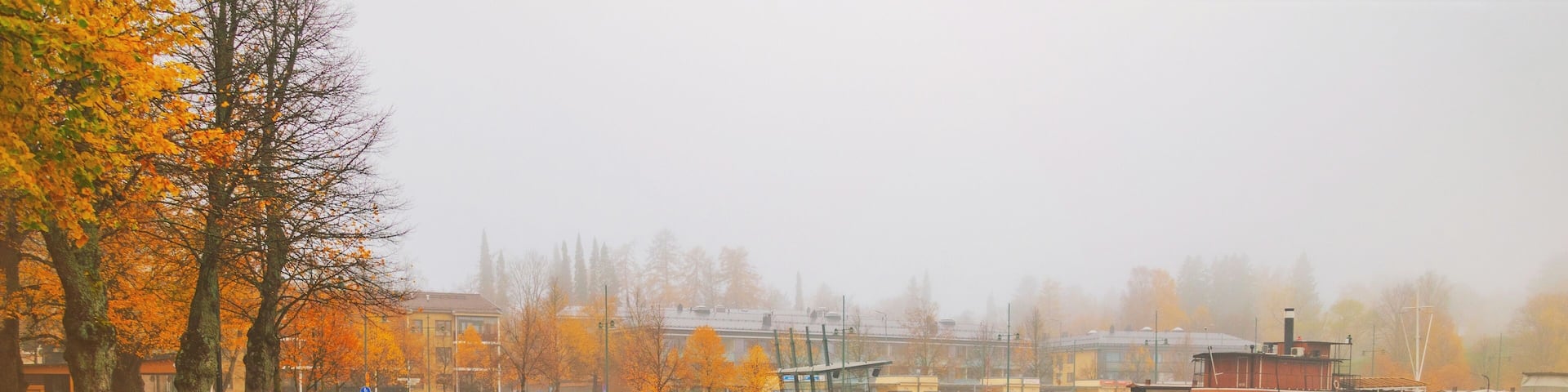 Lappeenranta port with boat at autumn day. Sights of Lappeenranta harbor and garden, beautiful fall tree yellow leaves amazing view. October autumn park foliage and lake fog scene, travel in Finland.