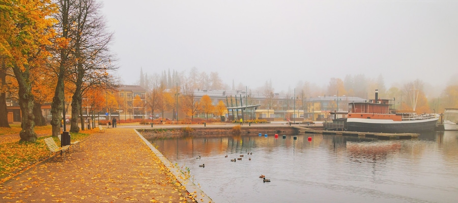 Lappeenranta port with boat at autumn day. Sights of Lappeenranta harbor and garden, beautiful fall tree yellow leaves amazing view. October autumn park foliage and lake fog scene, travel in Finland.