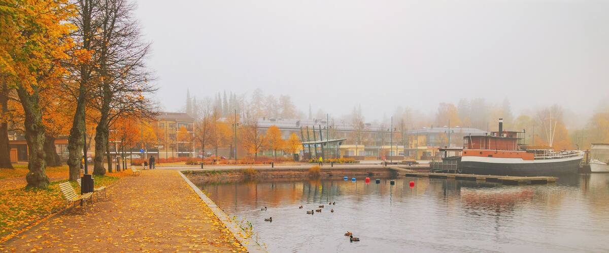 A foggy river with ducks, autumn leaves, and a boat docked on the right.