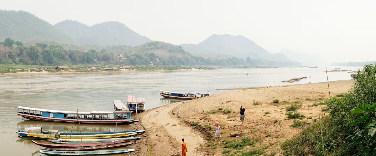 A river with boats, a sandy beach, and mountains in the background.