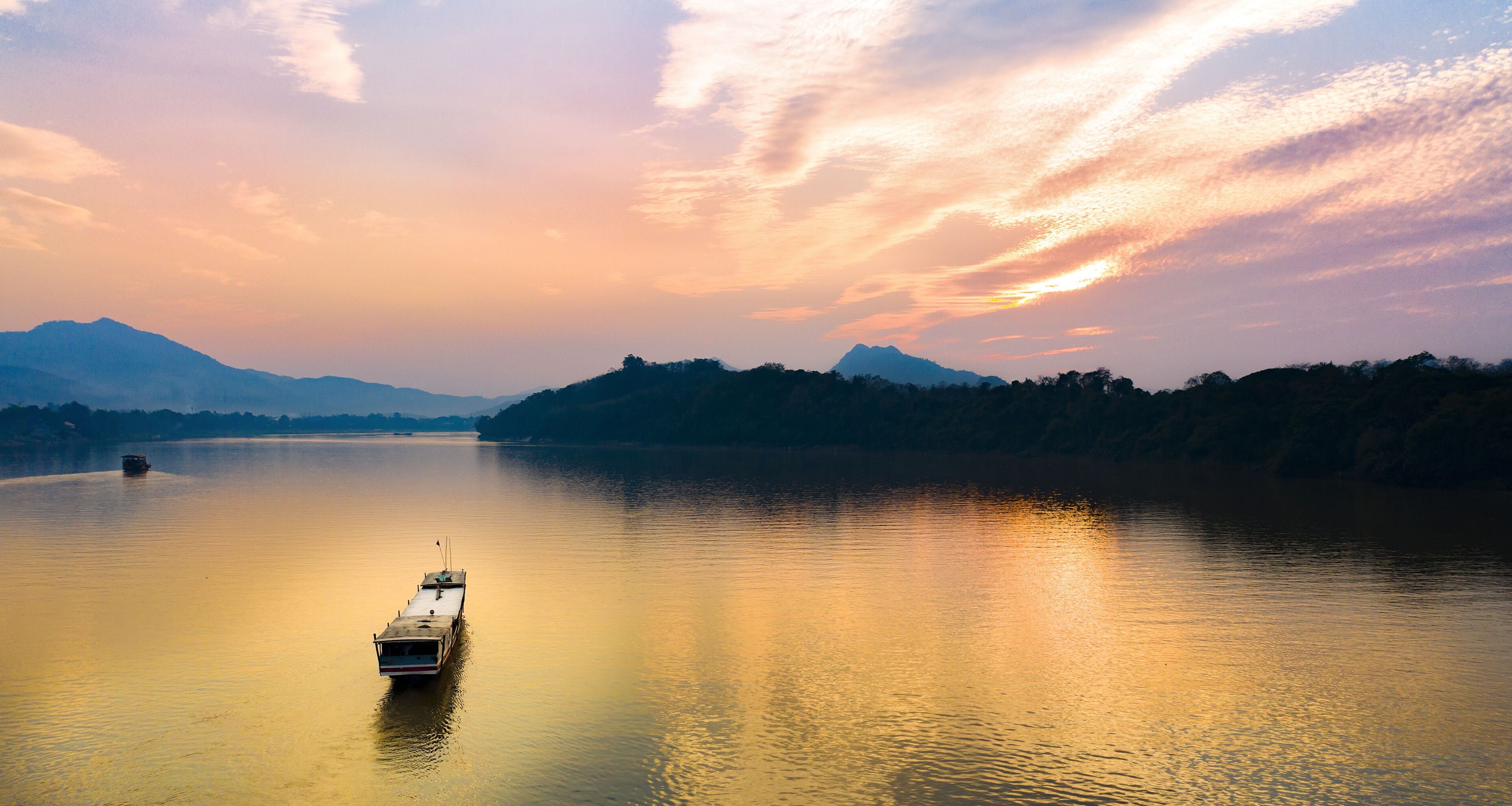 Stunning aerial view of a tourists boat sailing along the Mekong river at sunset in Luang Prabang, Laos.