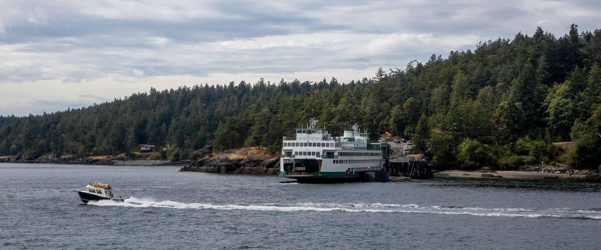 A Washington State Ferry unloading cars at Lopez Island ferry dock in the San Juan Islands as a fast powerboat cruises by.