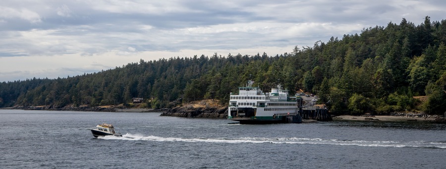 A Washington State Ferry unloading cars at Lopez Island ferry dock in the San Juan Islands as a fast powerboat cruises by.