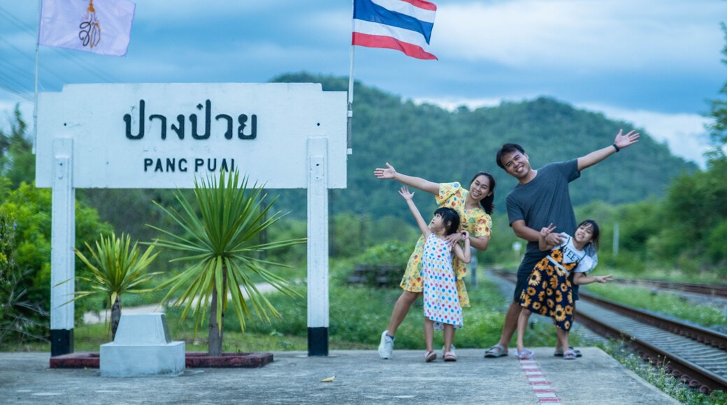 8 June 2023: Lampang, Thailand - Happy family taking pictures together at Pang Puai Railway Station against a background of green mountains and trees.