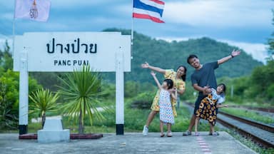 8 June 2023: Lampang, Thailand - Happy family taking pictures together at Pang Puai Railway Station against a background of green mountains and trees.