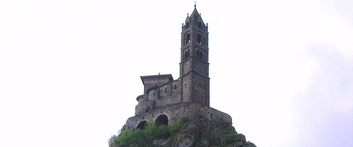 A large rocky hill with a church tower on top.