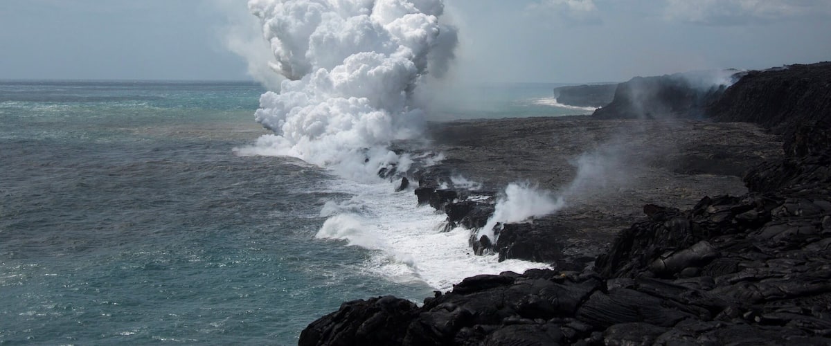 Una costa rocosa con olas rompiendo contra la orilla, generando espuma blanca y niebla.