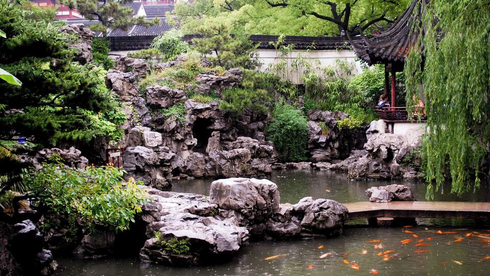 A traditional garden with a pond, rocks, koi fish, and a pavilion.